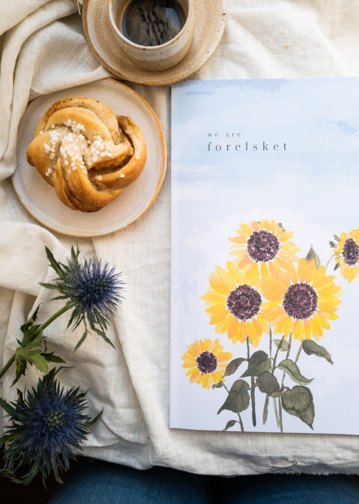 Magazin "we are forelsket" auf einer Decke mit Zimtschnecke, Kaffee und Blume